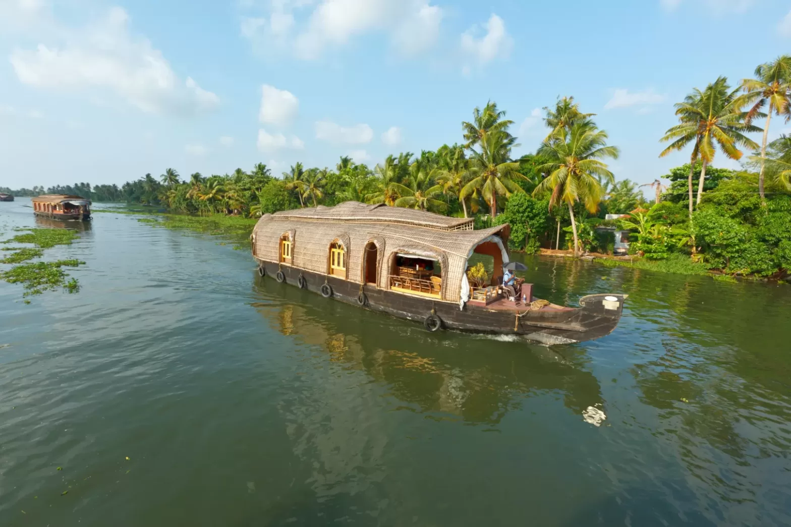 Traditional houseboat cruising through the serene backwaters of Kerala, India, surrounded by lush palm trees and greenery under a clear blue sky